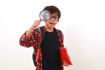 Happy smart asian student holding a book while looking through a magnifying glass. Isolated on white