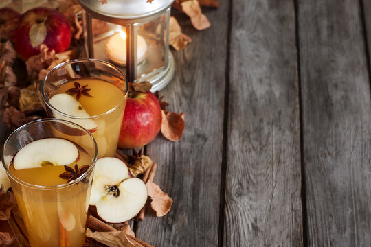 Hot apple cider with cinnamon sticks and spices on fall leaves background