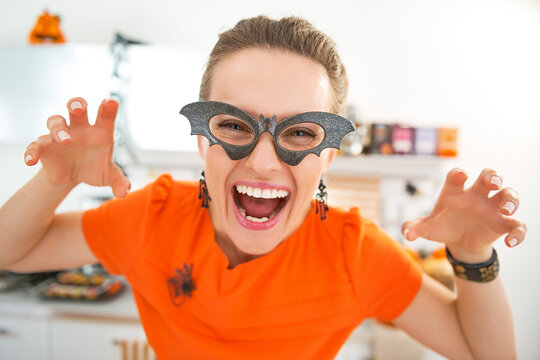 Frightful Treats all the way. smiling young woman in party bat glasses in the Halloween decorated kitchen frightening