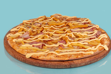 Pizza with bacon cheese and herbs on a wooden plate with cheese and cherry tomatoes. On a colored