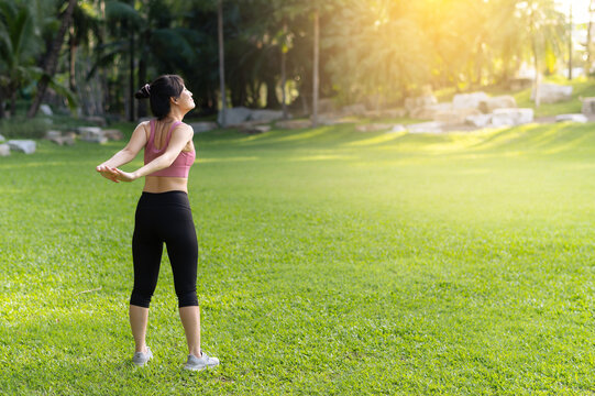 Female jogger. Get inspired fit active image of Asian young woman in pink sportswear stretching muscles in park before run, enjoying healthy outdoor activity. Wellness and fitness in natural setting.