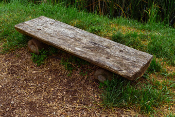 an empty old wooden bench from a log stands in the grass in summer