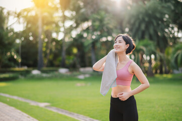 Fit and active 30s young Asian woman in pink sportswear wipes cheek after morning run in nature. Beauty of a healthy lifestyle and the sense of accomplishment that comes from achieving a fitness goal.