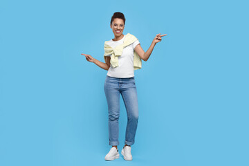 Happy young woman in stylish eyeglasses dancing on light blue background