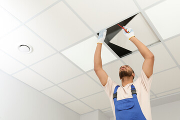 Electrician with screwdriver repairing ceiling light indoors, low angle view. Space for text - Powered by Adobe