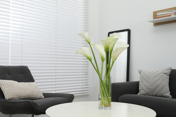 Beautiful calla lily flowers in glass vase on white table at home