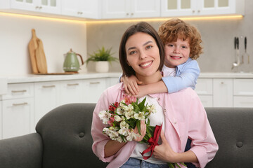 Little son congratulating his mom with Mother`s day at home, space for text. Woman holding bouquet of beautiful flowers