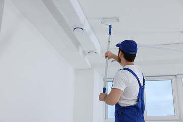 Handyman painting ceiling with roller in room, back view