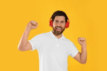 Happy man listening music with headphones on yellow background