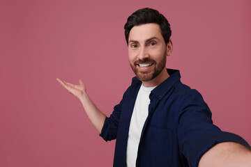 Smiling man taking selfie on pink background, space for text