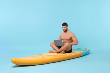 Man with laptop on SUP board against light blue background