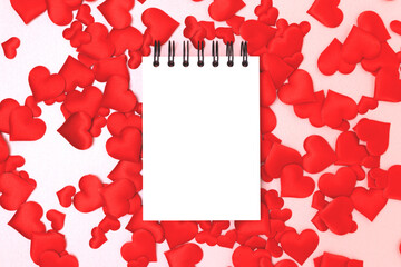 Blank notepad mockup and red textile hearts confetti on a pink glittering background. Festive creative concept.