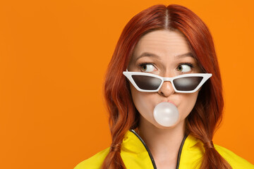 Emotional woman in sunglasses blowing bubble gum on orange background. Space for text