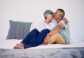 Love, kiss and senior couple on their bed in their home while relaxing, bonding and spending time together. Happy, affection and elderly man and woman in retirement resting in bedroom in their house.