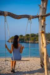 Young woman on wooden swing on Oludeniz beach. Summer holiday in Oludeniz, Turkey. Girl ride on a swing on sea coast, clear water. Travel concept