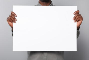 African American man holding sheet of paper on grey background, closeup. Mockup for design