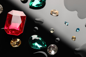 Different beautiful gemstones for jewelry on dark surface with drops