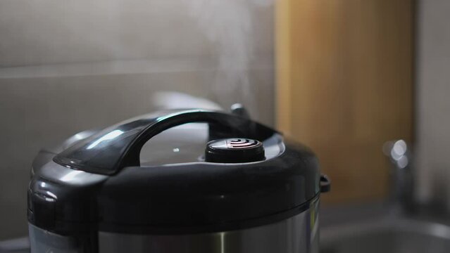 Close-up of steam escaping from nozzle of kitchen multicooker while cooking food in the kitchen. Electrical appliances for home and cuisine. Automatic multi cooker, pressure cooker. Rice maker brewing