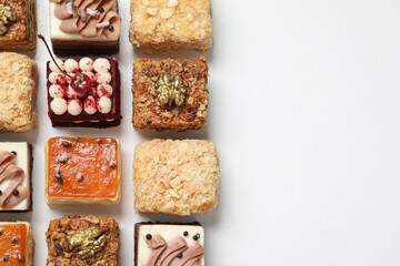 Pieces of different delicious cakes on white table, flat lay. Space for text