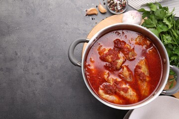 Delicious stuffed cabbage rolls cooked with homemade tomato sauce in pot and ingredients on grey table, flat lay. Space for text