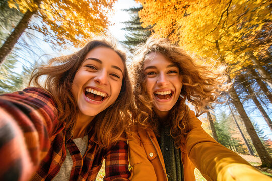 Two funny girls taking a selfie in a forest in autumn