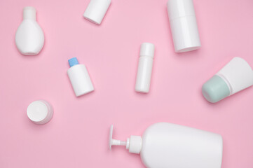 Still life. Flat lay. Various white small tester bottles with beauty products for skin and body care on pink background