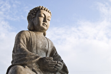 Sitting Buddha image in lotus position on sky background. Symbol of Buddhism religion