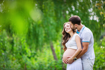 Happy young couple expecting baby in summer park