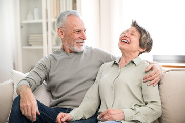 Laughing loving aged couple relaxing on cozy couch at home