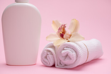 Obraz na płótnie Canvas Orchid flower on rolled tied white waffle towels, near a bottle with intimate hygiene gel, isolated on pink background