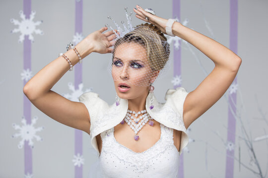 Beautiful young woman with purple makeup,  fancy hairdo and small crystal crown on head. Gorgeous winter bride in felting dress with surprised expression. Copy space.