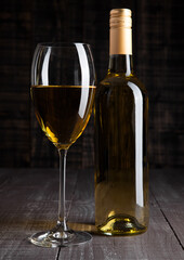 Bottle and glass of white wine on wooden board background