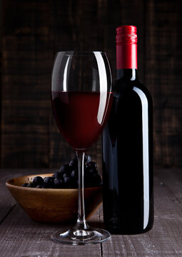 Bottle and glass of red wine with grapes in bowl on wooden board background