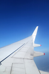 Wing of an airplane flying above the clouds on blue sky background