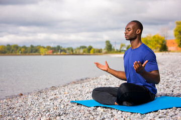 young black man wearing athletic wear sitting on the beach exercising yoga