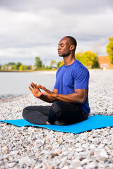 Naklejka na ściany i meble young black man wearing athletic wear sitting on the beach exercising yoga