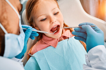 Close-up portrait of a little girl patient whose teeth are being checked by a dentist. Dental...