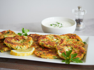 golden brown vegetable pancakes or fritters served with fresh parsley and lemon. In the background yourt sauce bowl and pepper shaker.