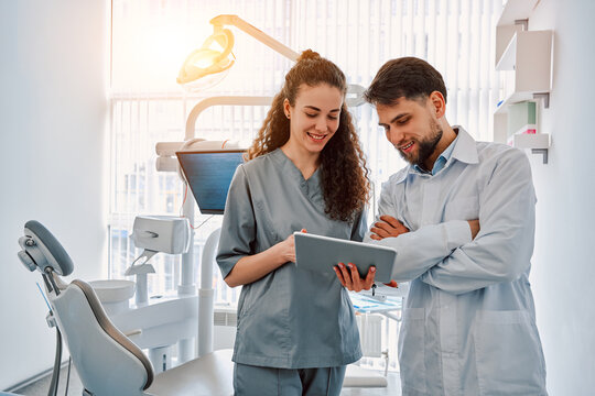 Two Dentist Doctors Are Standing In A Dental Office And Looking At A Tablet. Medicine, Dentistry.Sunlight.