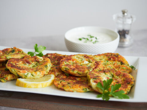 golden brown vegetable pancakes or fritters served with fresh parsley and lemon. In the background yourt sauce bowl and pepper shaker.