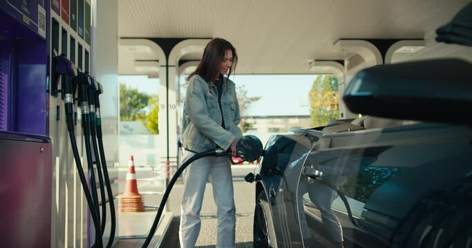 Portrait of a happy brunette girl who refuels her dark gray convertible. Refuel your car with joy