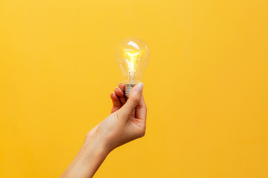 Close-up shot of a hand holding a glowing light bulb. creative business ideas Idea inspired by a light bulb on a yellow background. concept for success.