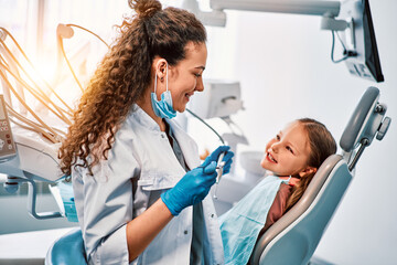 A female dentist doctor talks to a small patient, the child shows her teeth and sits in the dental chair.Sunlight.