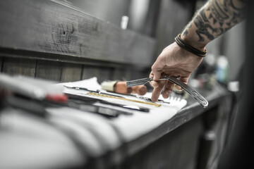 Guy's hand with a tattoo and a straight blade on the blurry background. Finger touches scissors...