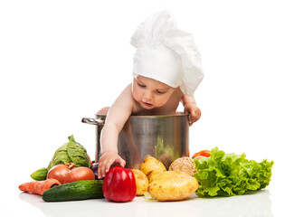 Little boy in chef's hat reaching for bell pepper while sitting in large casserole over white