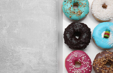 Box with different tasty glazed donuts on light grey table, top view. Space for text