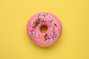 Fototapeta na wymiar Tasty glazed donut decorated with sprinkles on yellow background, top view
