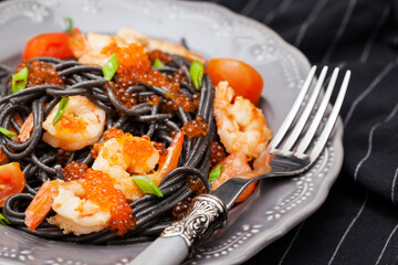Black spaghetti with shrimps and red caviar on dark background