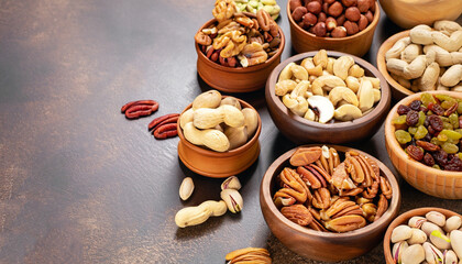 Assortment of nuts in wooden bowls. Cashew, hazelnuts, walnuts, pistachio, pecans, pine nuts, peanut, raisins. Food mix background, top view, copy space, banner.