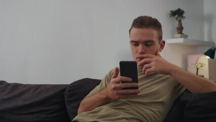 Young Man Sits on Couch and Stares at Phone, Concept Digital Connectivity, Social Media and Connectivity, Dependence on Technology  - Powered by Adobe